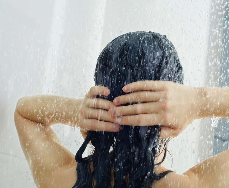 girl seen from behind the shower while she washes her hair